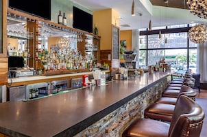 Zona de bar con una barra alargada, numerosas botellas de licor y una variedad de vasos.