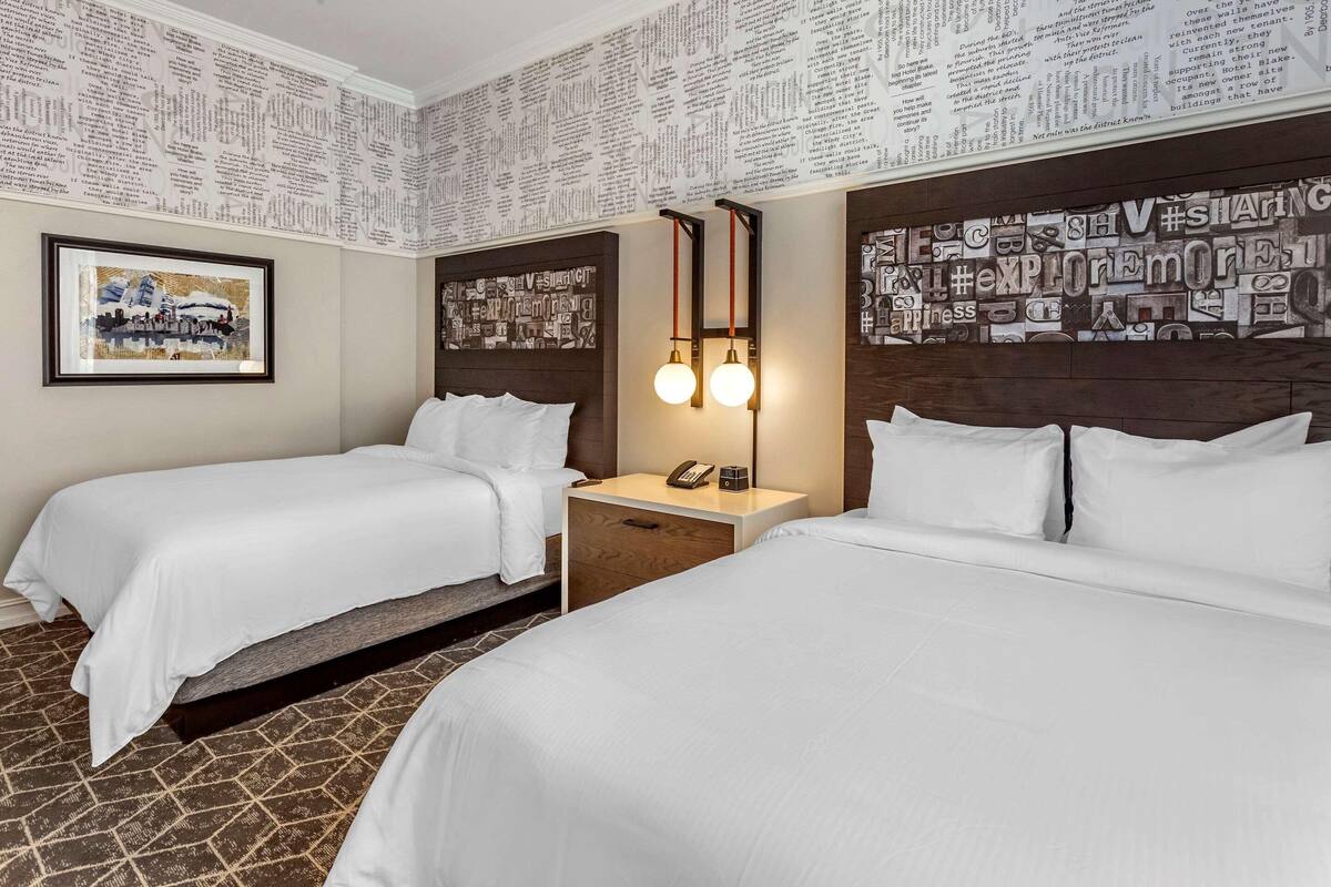 A hotel room with two beds, a nightstand with a phone, and a wall with printed text.