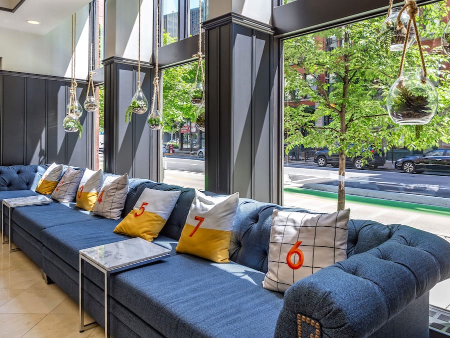 Een moderne hotel lobby met een lange blauwe bank, genummerde kussens en hangende plantenbakken.