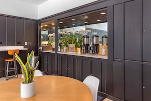 Una sala de conferencias moderna con una mesa de madera, sillas blancas, una planta en maceta y un amplio ventanal con plantas decorativas.