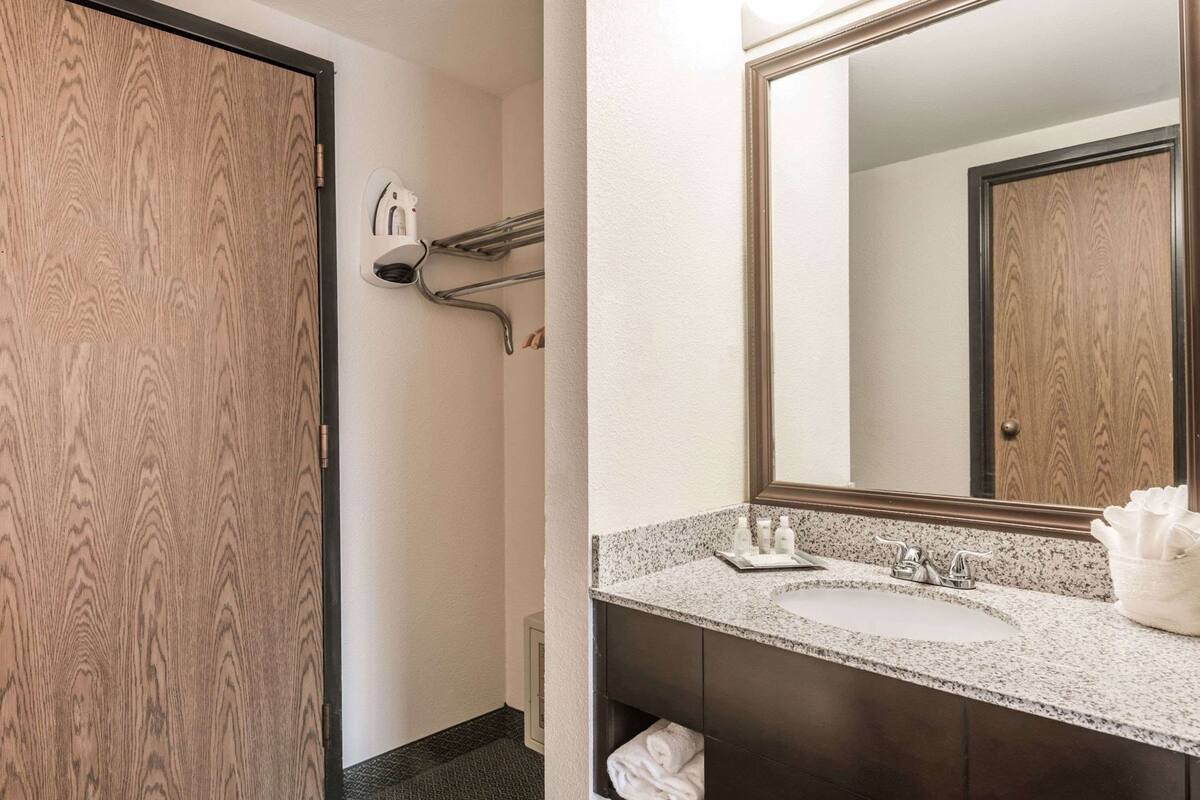 A bathroom with a wooden door, a towel rack, a mirror, a sink, and toiletries.