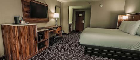 Habitación de hotel con cama, escritorio con televisor y alfombra estampada.