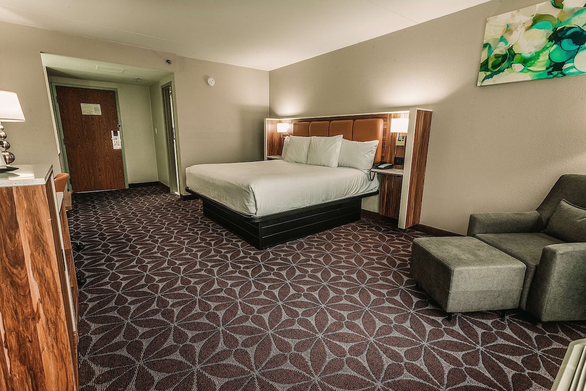 A hotel room with a large bed, a desk with a lamp, a chair, and a patterned carpet.