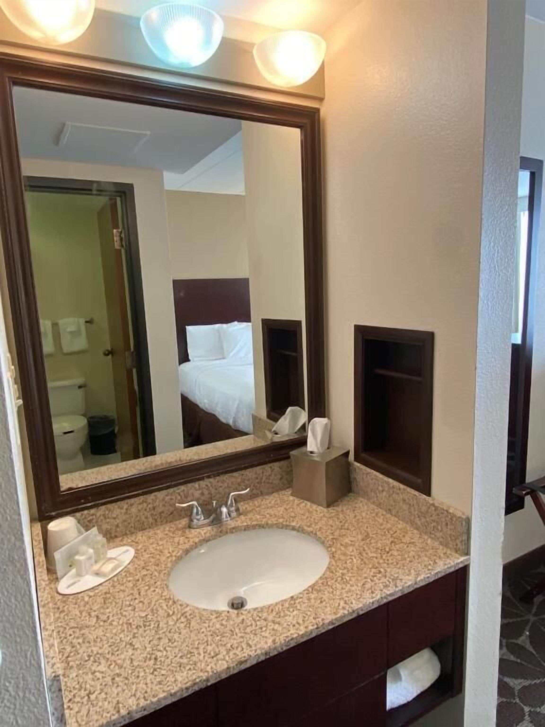 A hotel bathroom with a large mirror, a sink, and a toilet visible in the reflection.