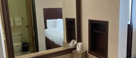 Ein Hotelbad mit einem großen Spiegel, einem Waschbecken und einer Toilette, die sich im Spiegelbild zeigen.