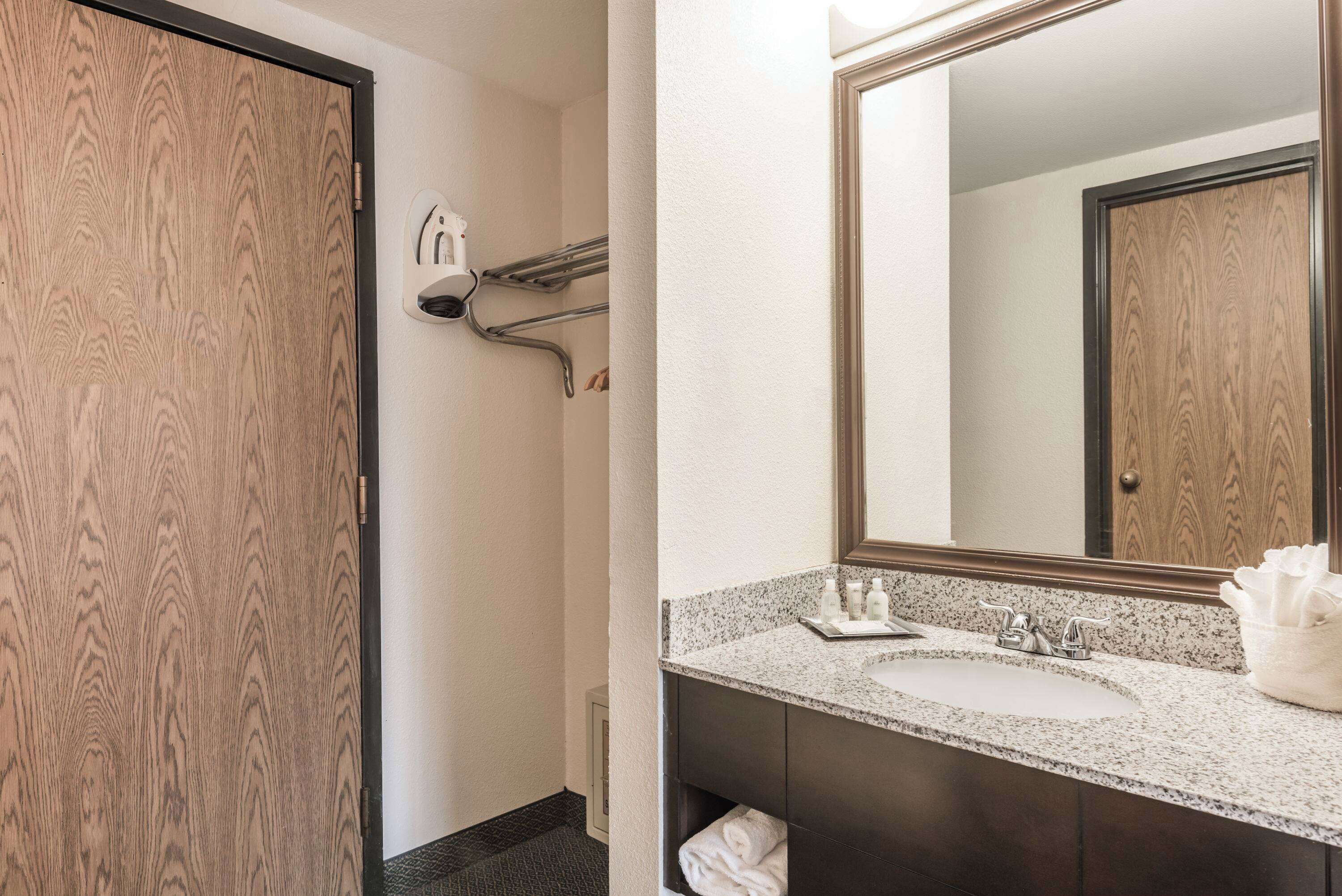 A bathroom with a wooden door, a sink with a mirror, and towel racks.