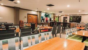 A modern dining area with multiple tables and chairs, wooden and cushioned seating, and a large window with a view.