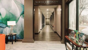 A hotel corridor with a marble floor, a table with a lamp, a bench with brochures, and a large window with a view.