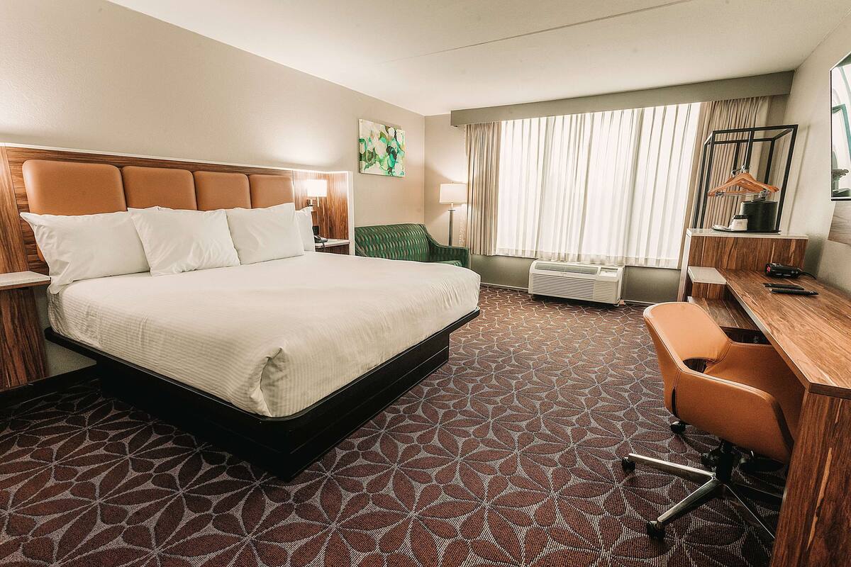 A hotel room with a large bed, a desk, a chair, a lamp, and a window with curtains.