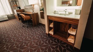 A hotel room with a desk, chair, and a vanity with a mirror.