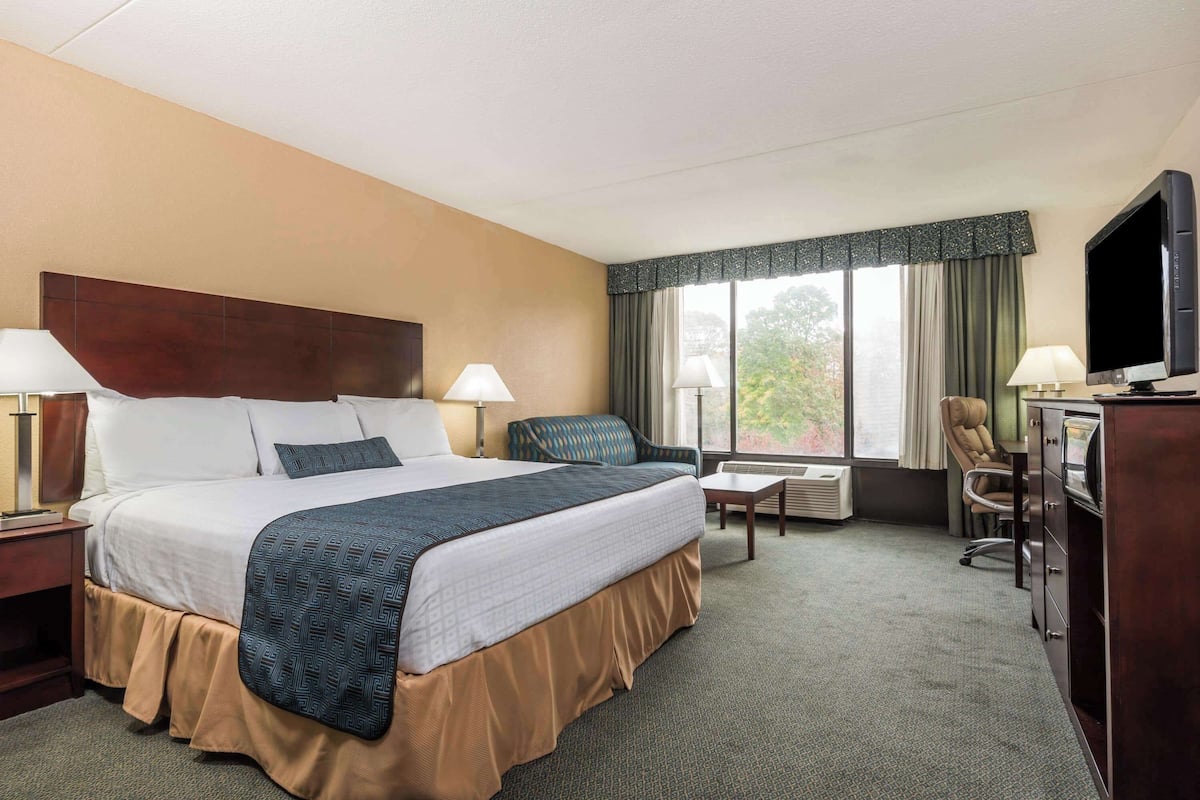 A hotel room with a large bed, two bedside tables with lamps, a desk with a chair, a television, and a window with curtains.