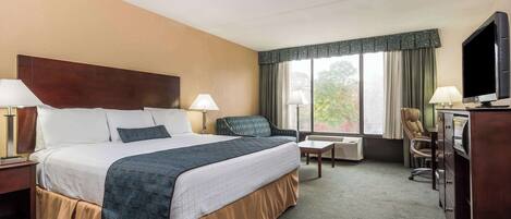 A hotel room with a large bed, two bedside tables with lamps, a desk with a chair, a television, and a window with curtains.