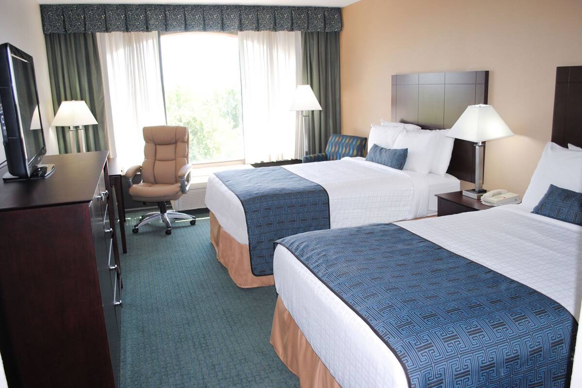 A hotel room with two beds, a desk with a computer, a chair, and a window with curtains.