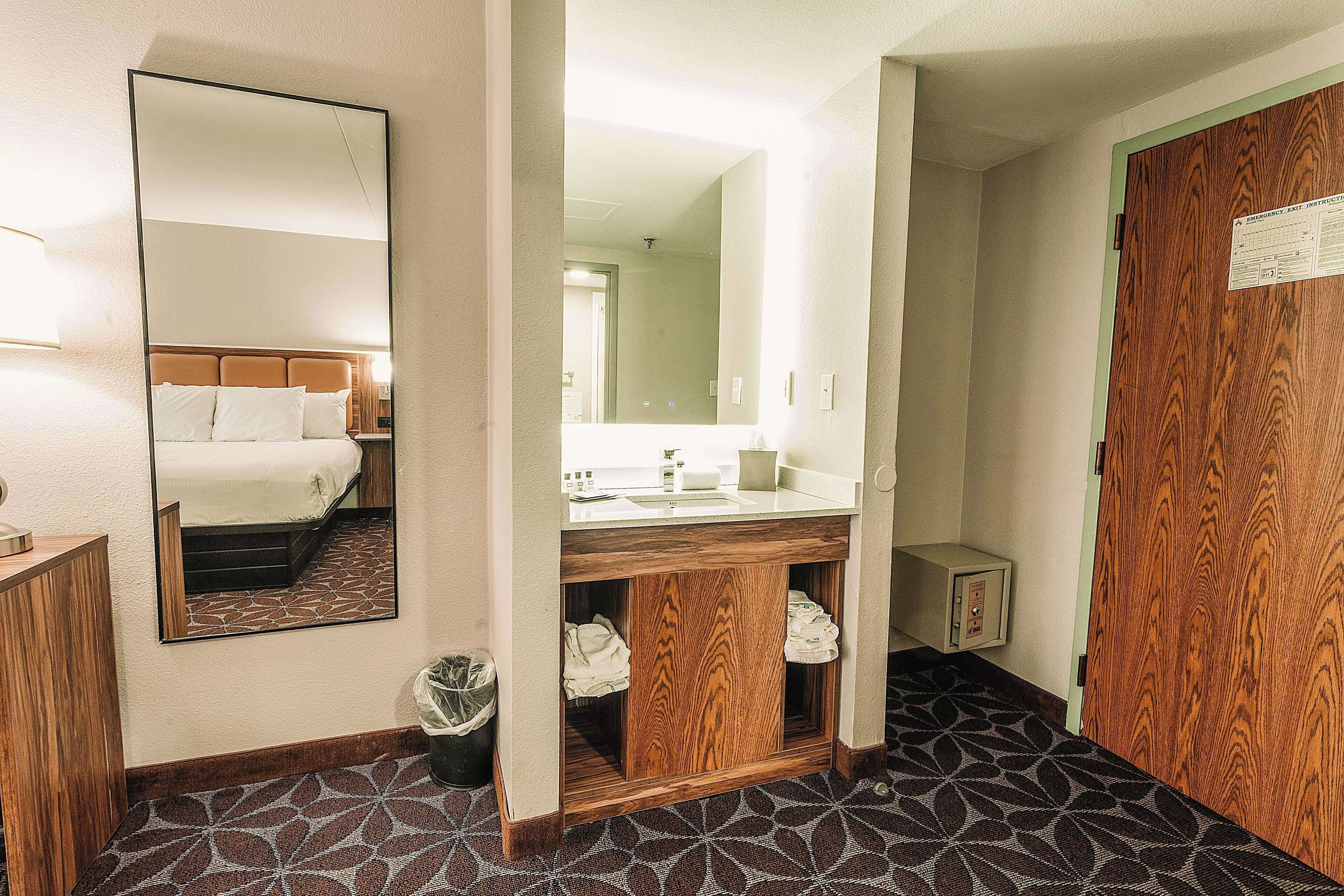 A hotel room with a bed, a large mirror, a wooden cabinet, and a sink.