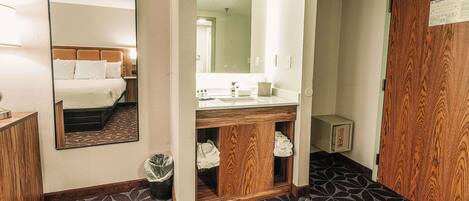 A hotel room with a bed, a large mirror, a wooden cabinet, and a sink.