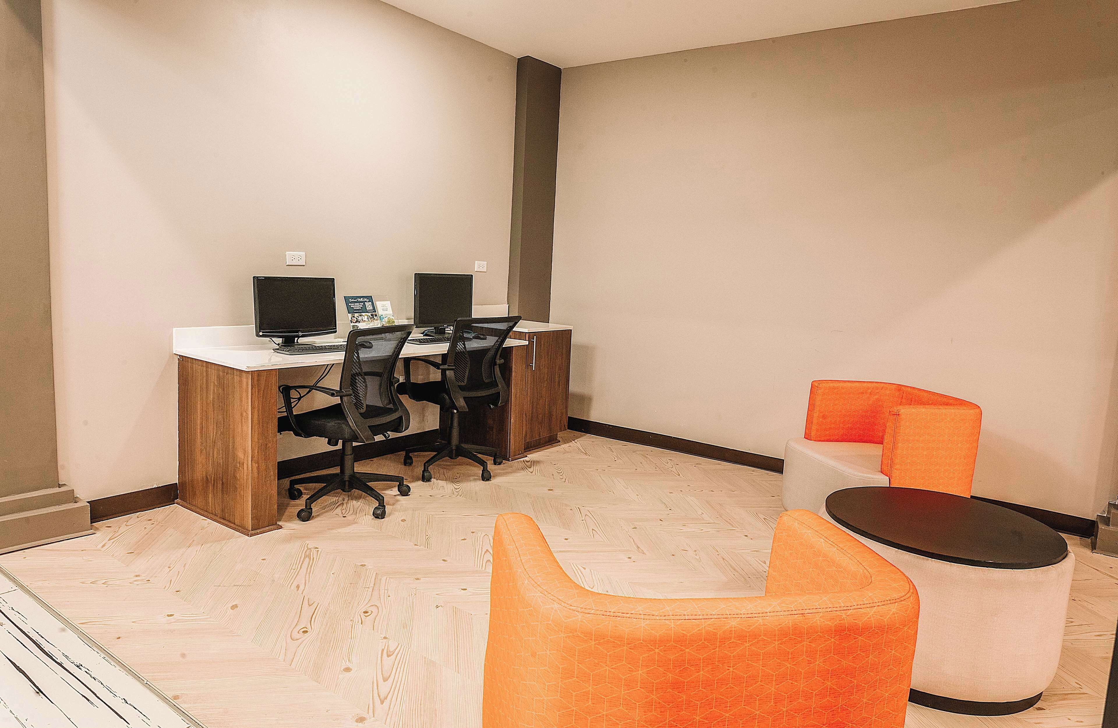 A modern office space with a wooden desk, two monitors, and orange seating.