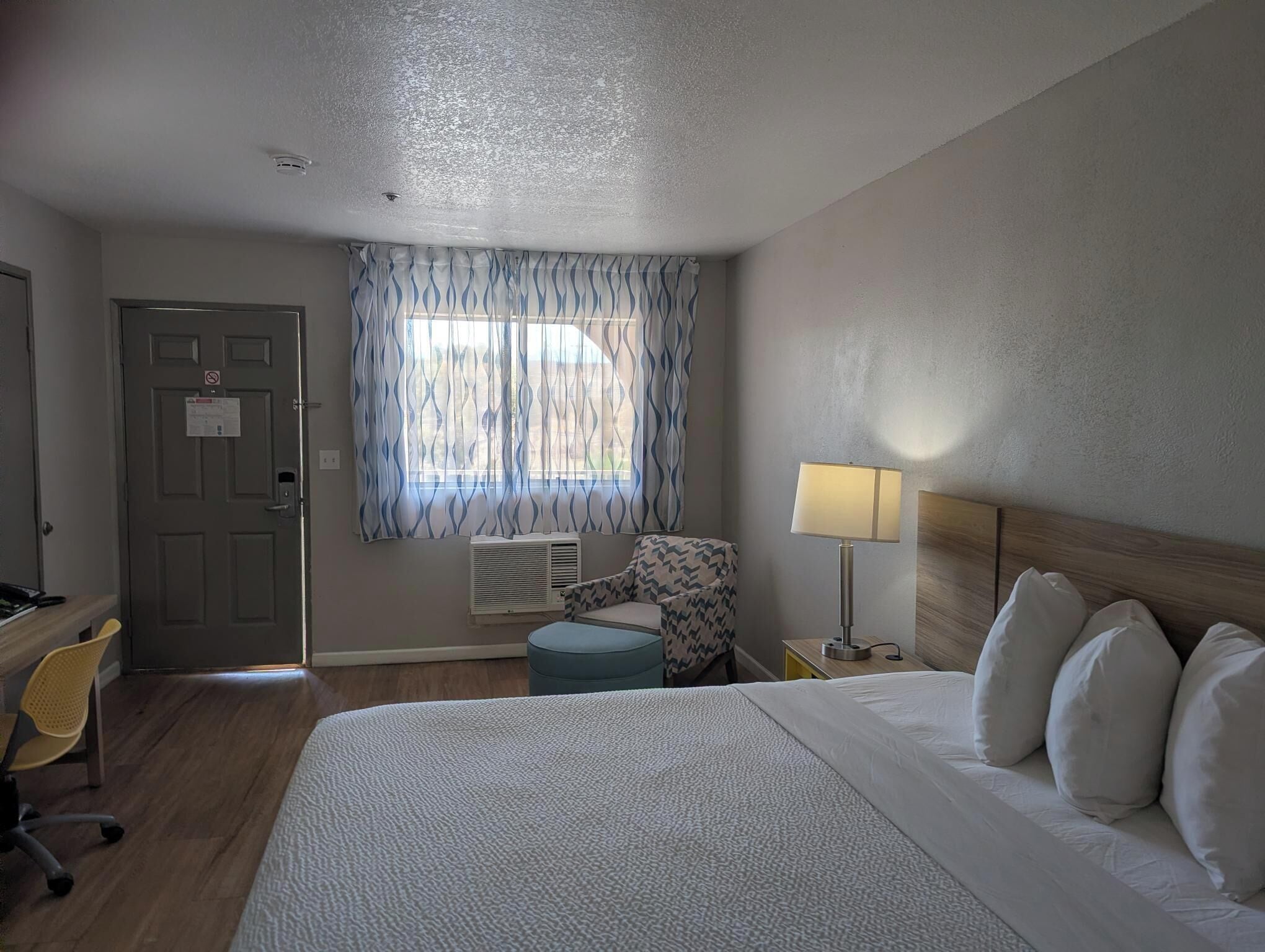 Een hotelkamer met een bed, een stoel, een bureau en een raam met gordijnen.