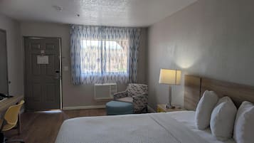 A hotel room with a bed, a chair, a desk, and a window with curtains.