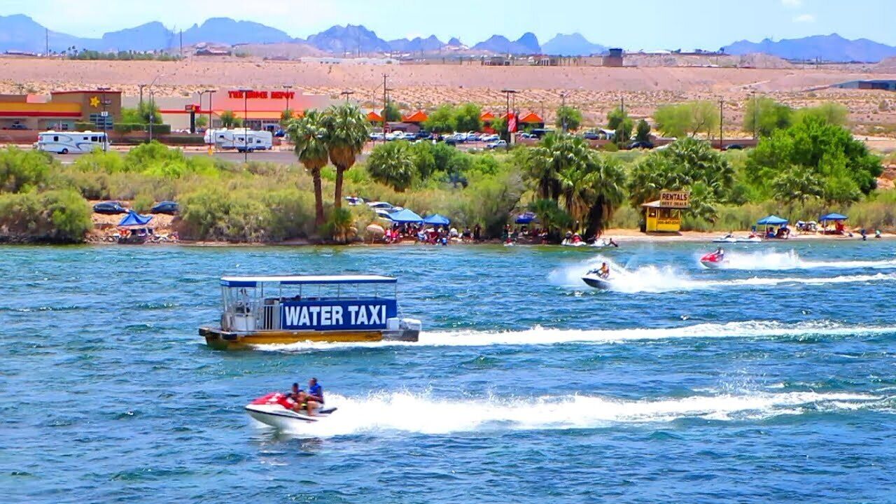 Un servicio de taxi acuático en un lago, con una tienda de alquiler y un paisaje desértico al fondo.