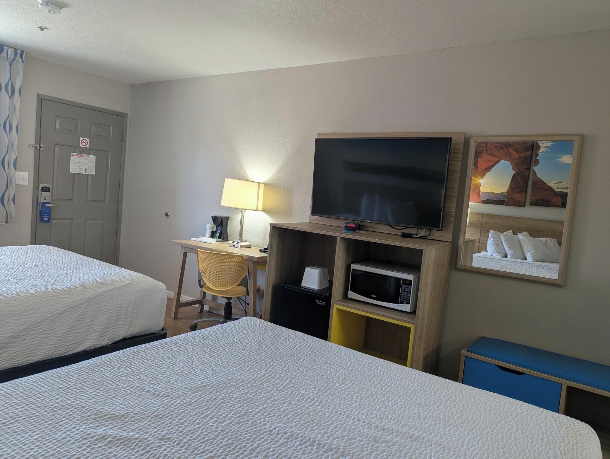 A hotel room with two beds, a desk with a lamp, a flat-screen TV, a microwave, and a painting on the wall.