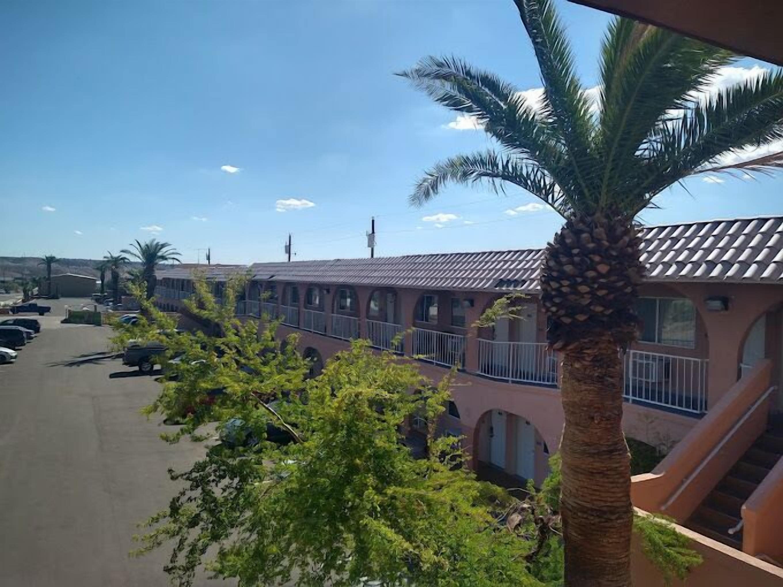 A hotel with a parking lot, palm trees, and a building with a tiled roof.
