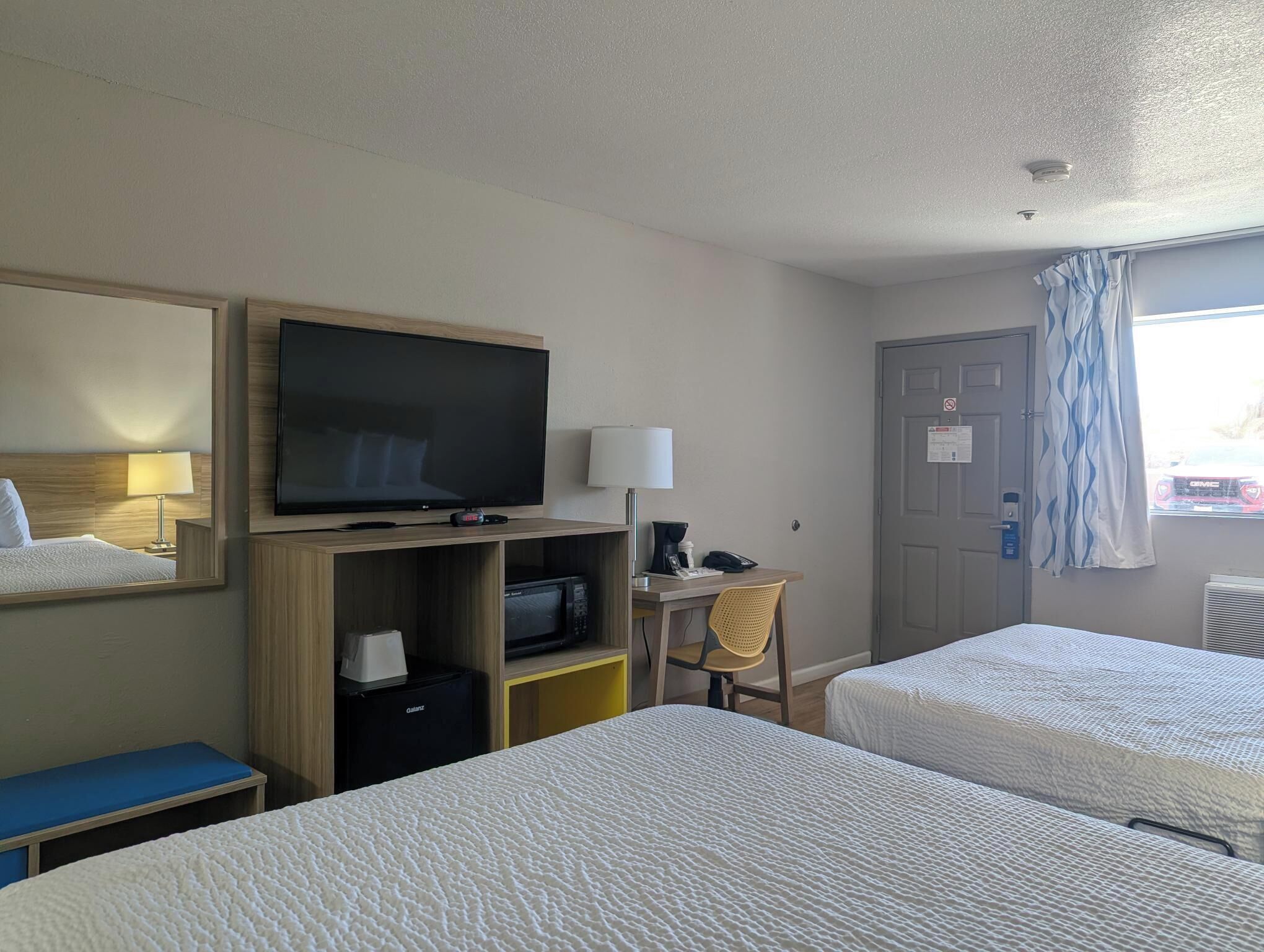 Habitación de hotel con dos camas, una televisión, un escritorio con lámpara y una ventana con cortinas.