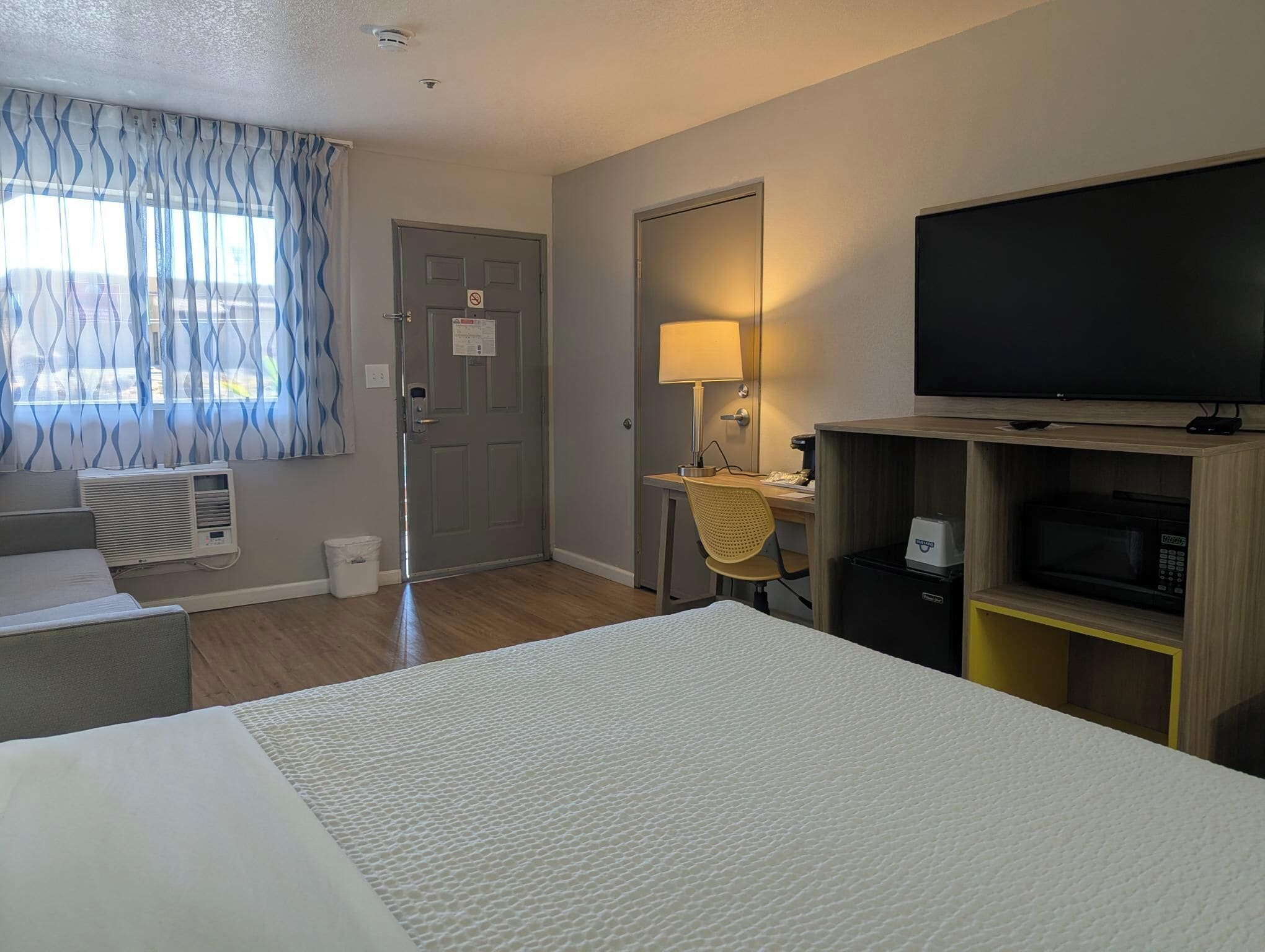 Habitación de hotel con cama, escritorio con lámpara, televisor y microondas.