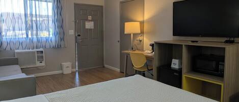 Habitación de hotel con cama, escritorio con lámpara, televisor y microondas.