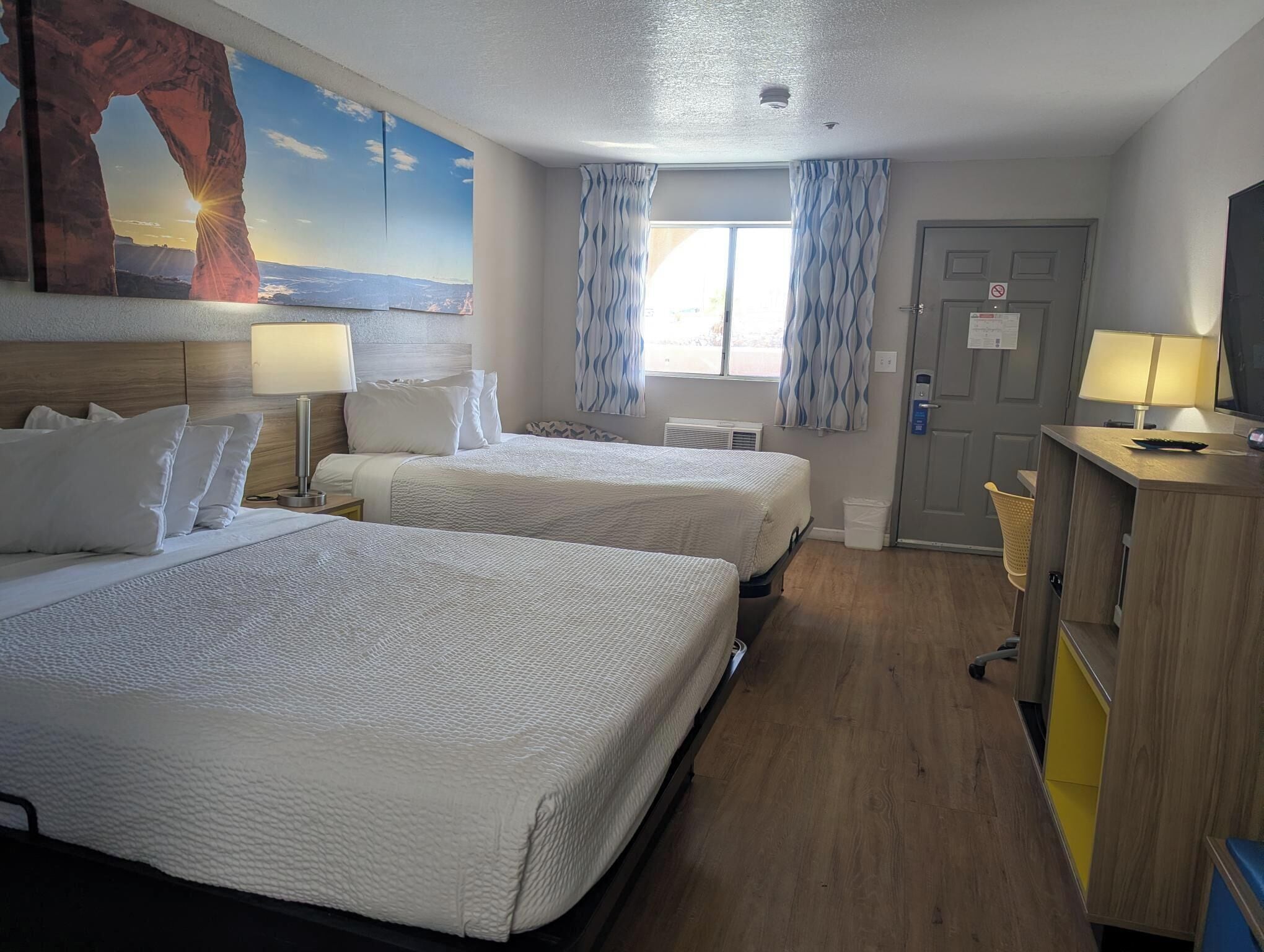 A hotel room with two beds, a desk, a television, and a window with curtains.