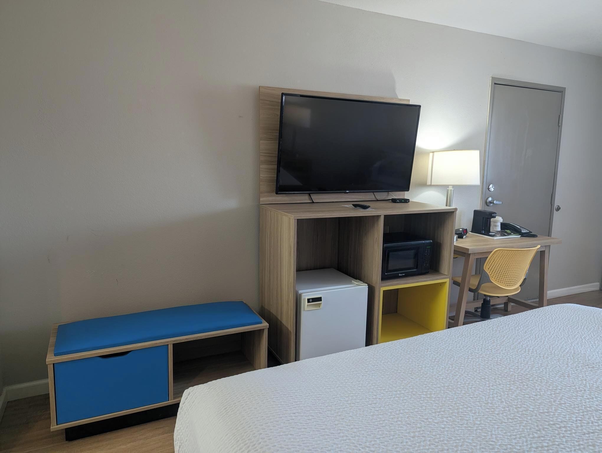 Habitación de hotel con cama, escritorio y silla, televisor, microondas y refrigerador pequeño.