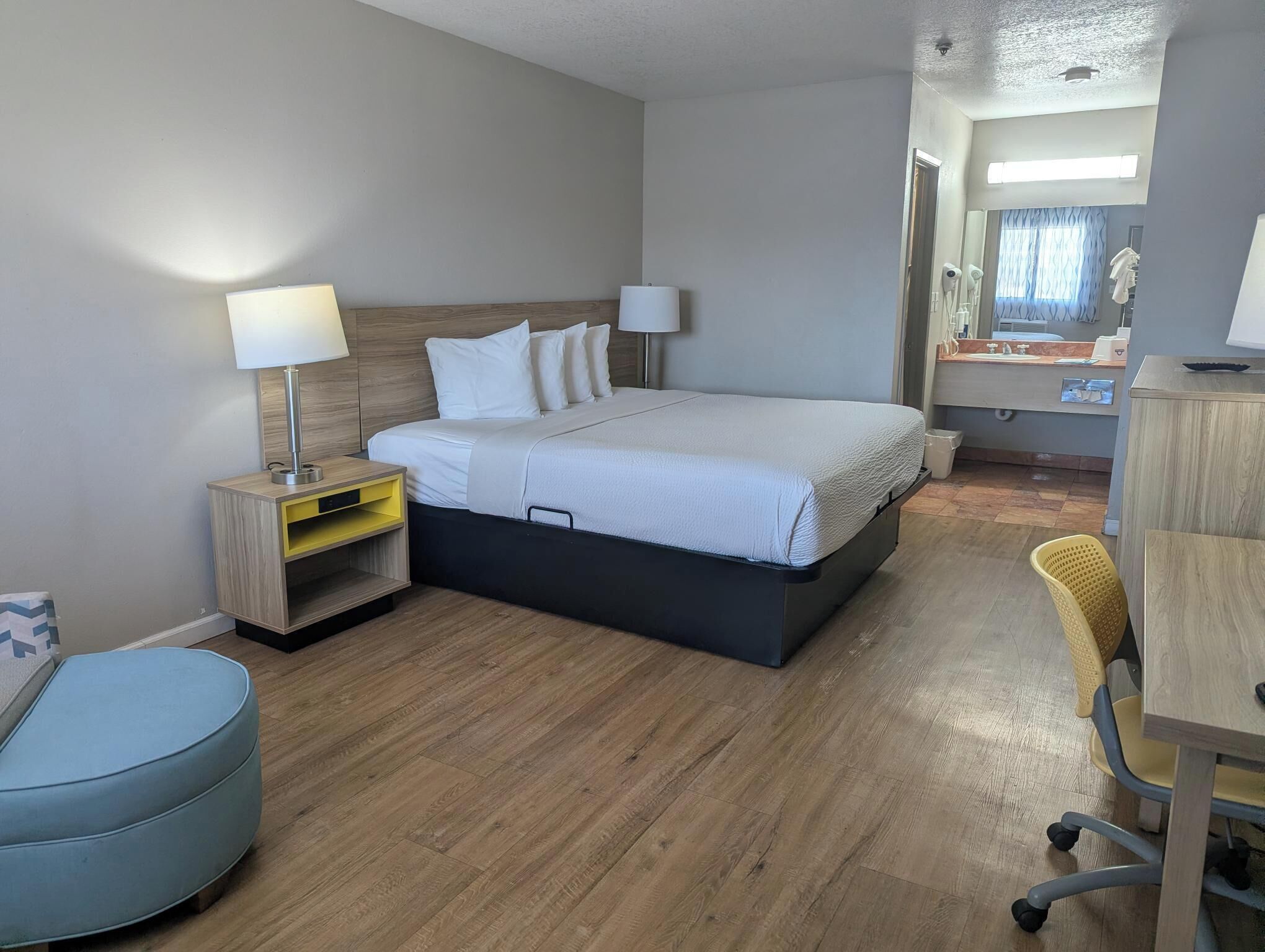 Quarto de hotel com cama, mesas de cabeceira, escrivaninha, cadeira e banheiro visível por uma porta aberta.