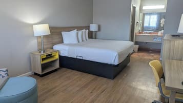 A hotel room with a bed, bedside tables, a desk, a chair, and a bathroom visible through an open door.