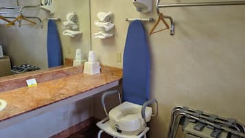 A bathroom with a marble countertop, a sink, a mirror, a hand dryer, a towel rack, a grab bar, and a wheelchair-accessible toilet.