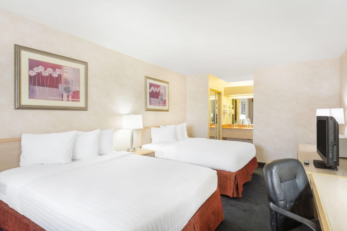 A hotel room with two beds, a desk with a computer, and a TV.