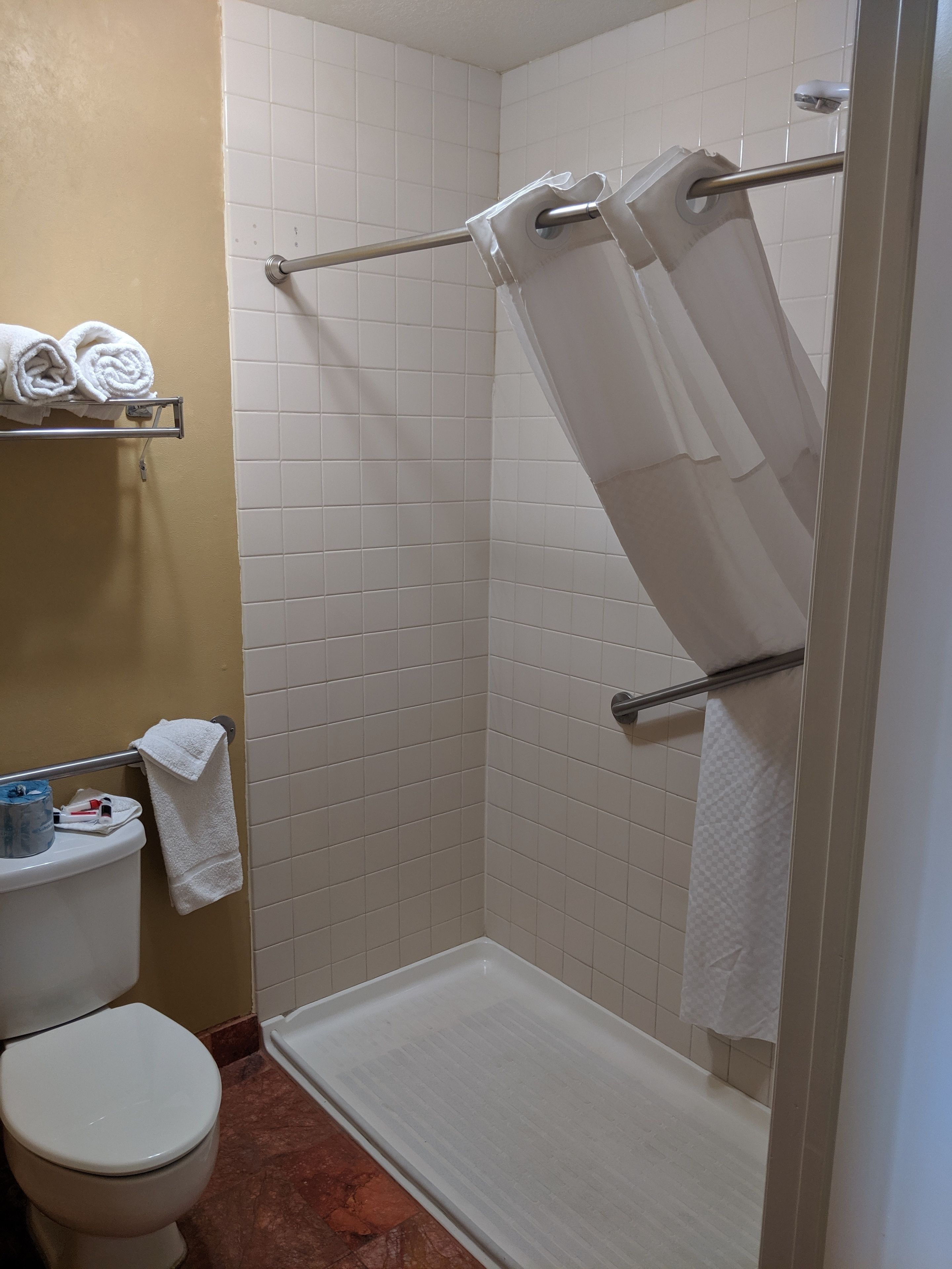 A bathroom with a shower, toilet, and a shelf with towels.