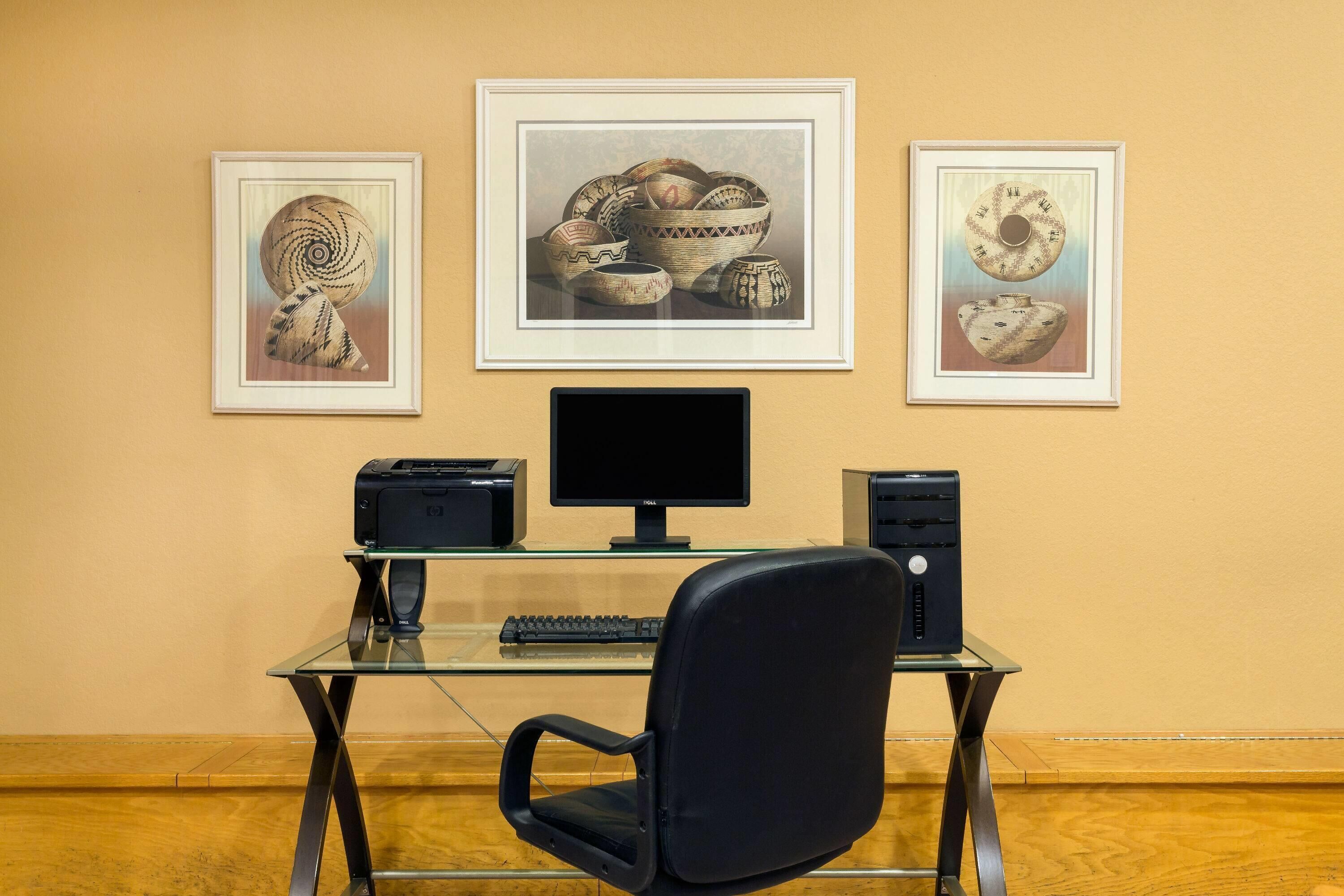 A workspace with a glass desk, a black chair, a computer monitor, a keyboard, and two printers.