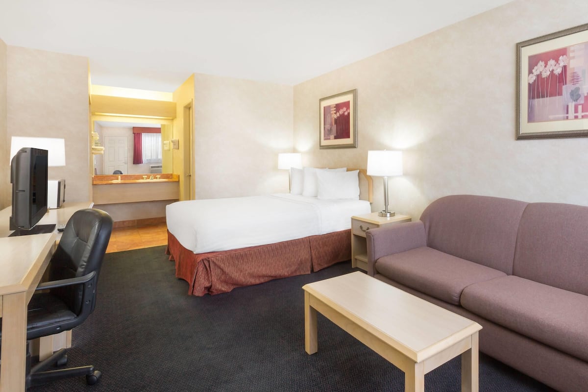 A hotel room with a bed, a desk with a computer, a sofa, a small table, and a mirror.