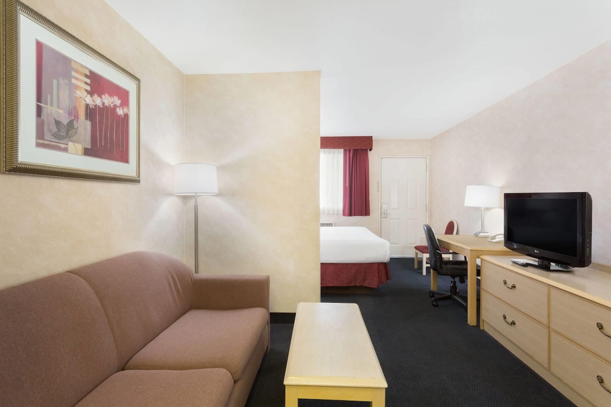 A hotel room with a sofa, a small table, a TV, a desk with a computer, a chair, and a bed with a red bedspread.