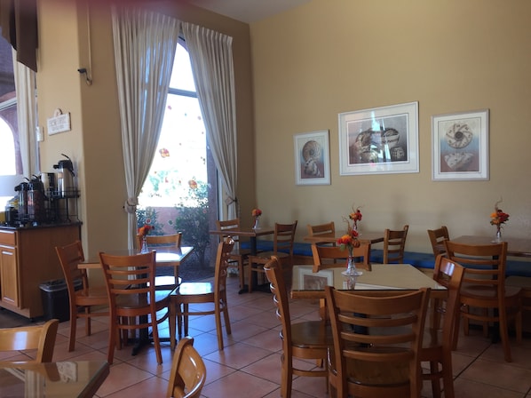 A dining area with wooden chairs and tables, a coffee station, and framed artwork on the walls.