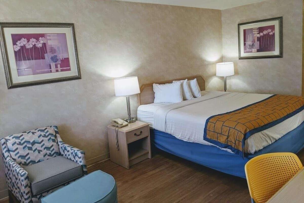 A hotel room with a bed, two bedside tables, a chair, and two framed pictures on the walls.