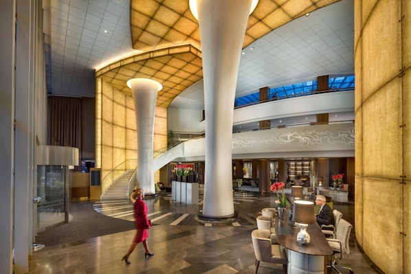 A spacious lobby with high ceilings, large columns, a central staircase, and a seating area with tables and chairs. - Kempinski Hotel Corvinus Budapest (Budapest)