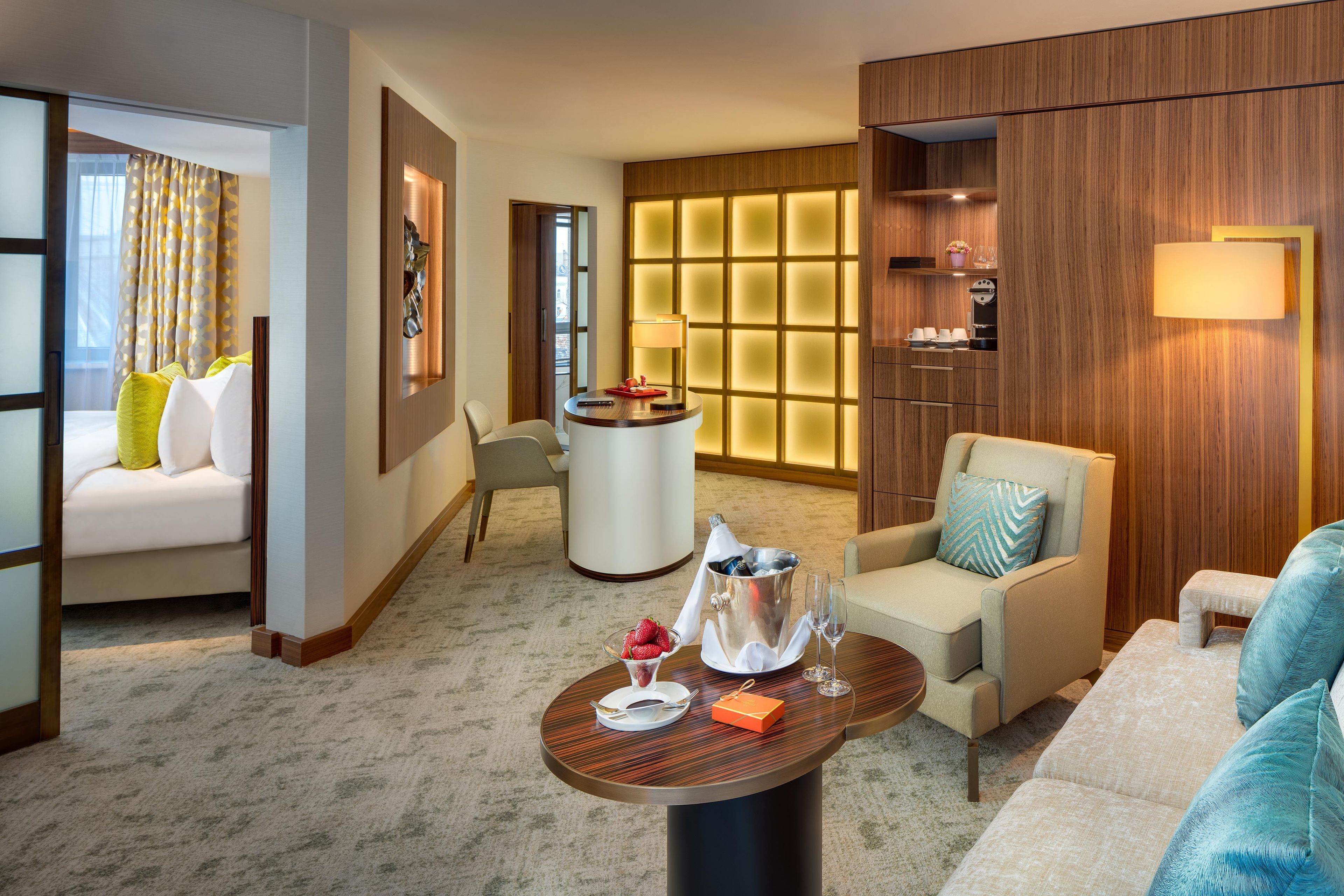 Quarto de hotel com área de estar, uma pequena mesa com uma garrafa de champanhe e um minibar.