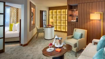 Quarto de hotel com área de estar, uma pequena mesa com uma garrafa de champanhe e um minibar.