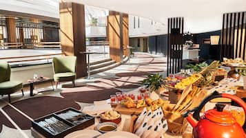 Un moderno vestíbulo de hotel con zona de comedor que incluye un bufé, diferentes disposiciones de asientos y una estación de café.