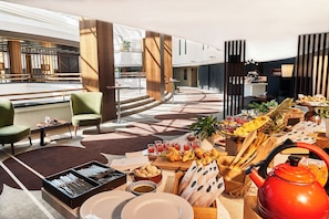 Un moderno vestíbulo de hotel con zona de comedor que incluye un bufé, diferentes disposiciones de asientos y una estación de café.