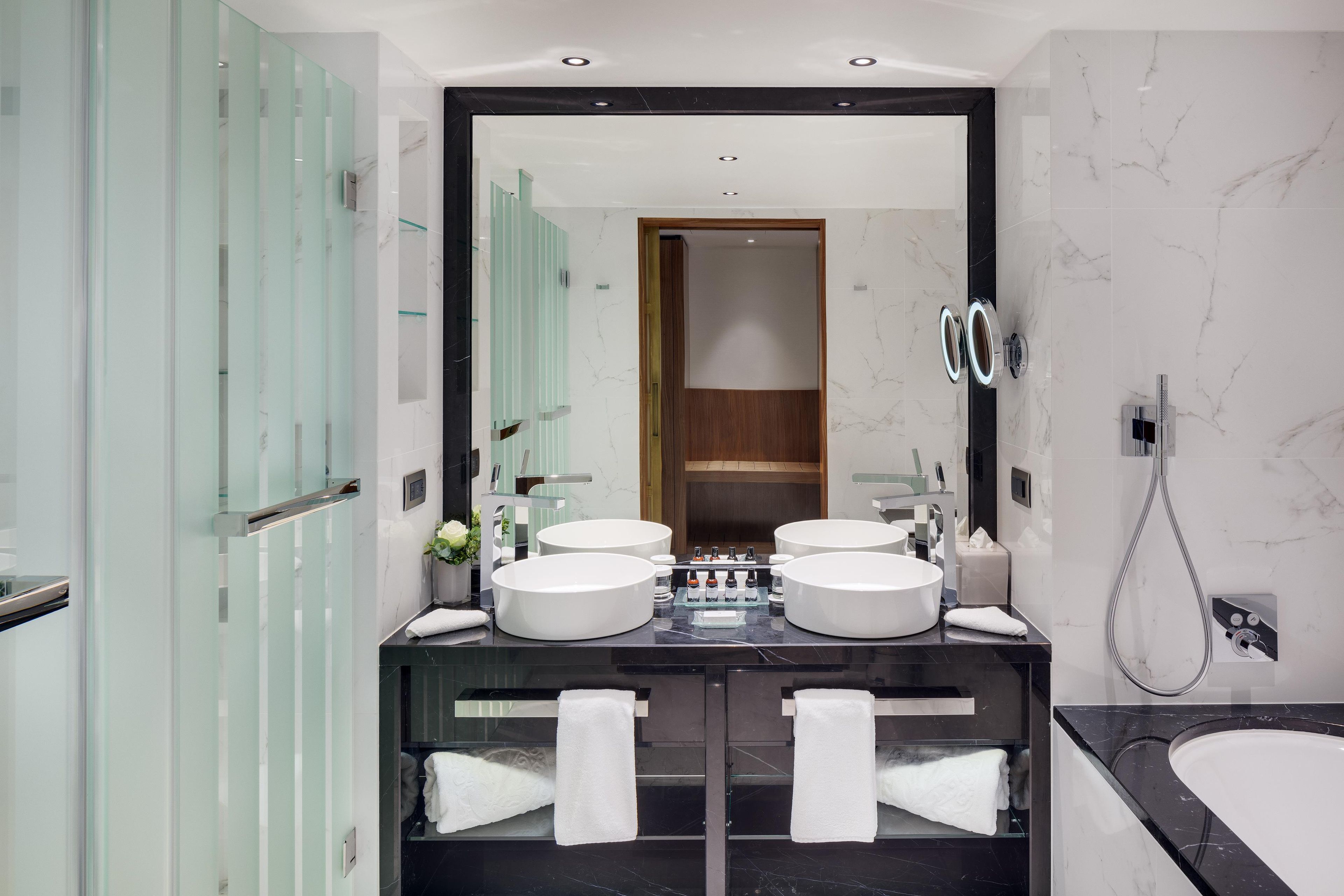 Un baño moderno con dos lavamanos, cabina de ducha con mampara de vidrio y un espejo grande.
