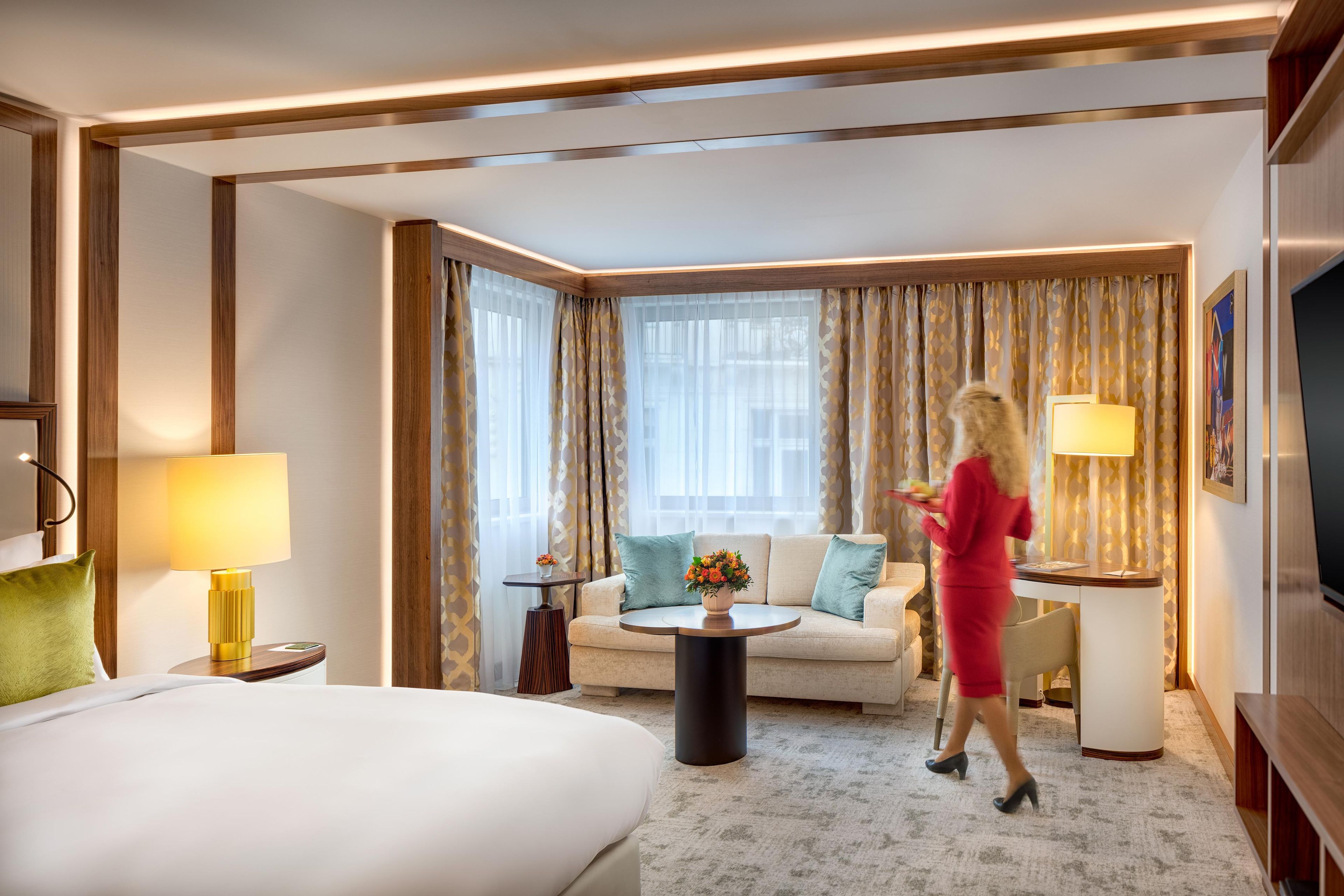 Una habitación de hotel con cama, sofá, mesa de centro, televisor y lámpara.