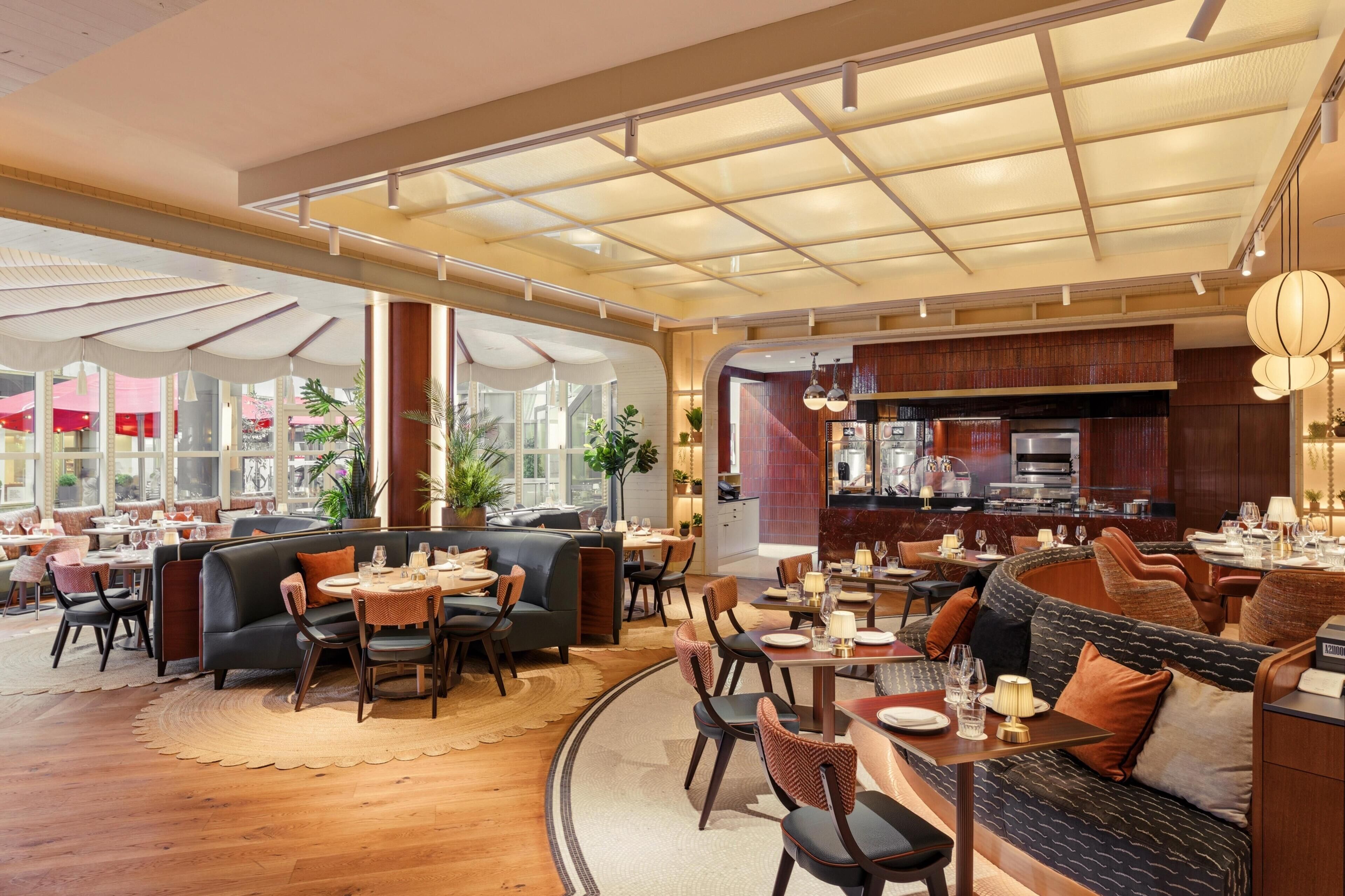 A spacious restaurant with high ceilings, large windows, and a variety of seating options including booths and tables.