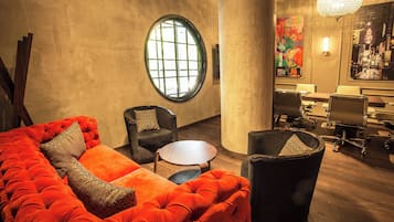 A modern interior with a large red sofa, two armchairs, a round wooden table, and a meeting area with chairs and a desk.