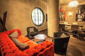 Un interior moderno con un sofá rojo grande, dos sillones, una mesa redonda de madera y una zona de reuniones con sillas y un escritorio.